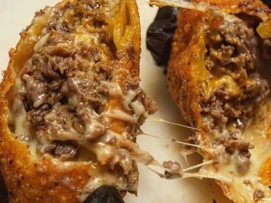 Cheesesteak egg rolls cut open with a cheese pull