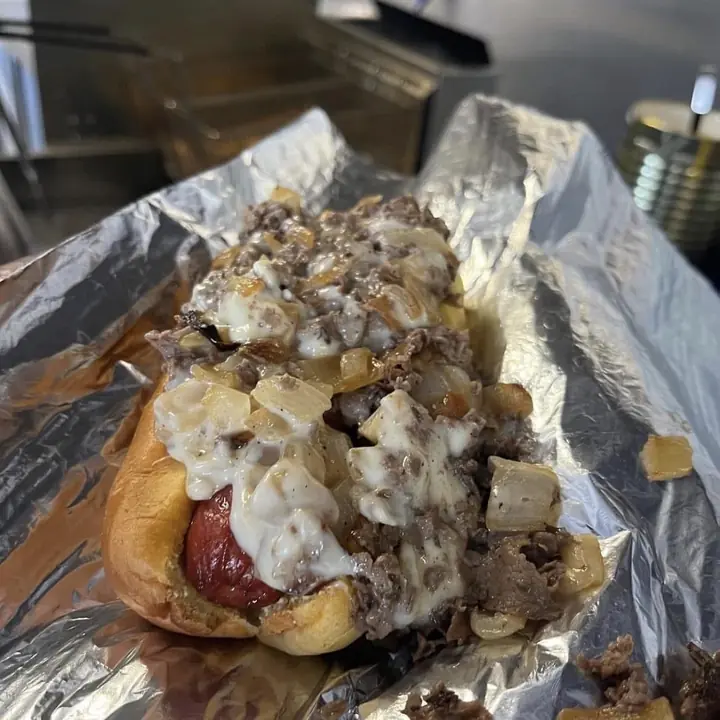 A hot dog topped with chopped cheesesteak, onions and cheese